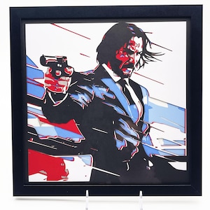 May include: Framed artwork featuring a stylized portrait of a man in a suit holding a gun. The artwork uses red, blue, and black colors against a white background. The image is in a black frame and displayed on a clear stand.
