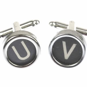 Può includere: Un paio di gemelli d'argento con tasti di macchina da scrivere in bianco e nero. I tasti presentano le lettere "U" e "V".