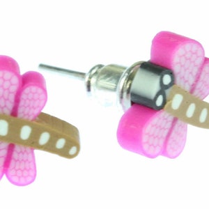 Op de afbeelding: Een paar roze libellen oorbel studs met bruine en witte accenten. De oorbellen hebben een zilveren pin en een vlinder achterkant.