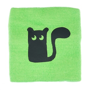 May include: A green knitted wristband with a black cat design. The cat has large eyes and a long tail.