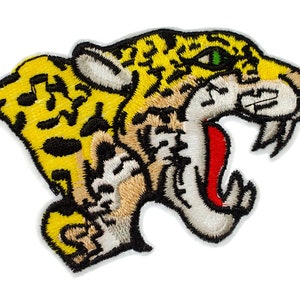 May include: An embroidered patch of a yellow and black jaguar head with a red open mouth and green eyes.