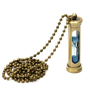 Può includere: Una collana con clessidra dorata con una clessidra di sabbia blu. La collana ha una catena a pallini.