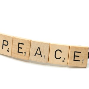 May include: The word "PEACE" spelled out using five wooden letter tiles from a Scrabble game. Each tile has a letter and a point value.