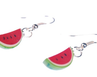 May include: A pair of watermelon slice earrings. Each earring features a red watermelon slice with black seeds and a green rind. The earrings have silver-colored fish hook ear wires. The earrings are set against a white background.