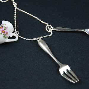 Può includere: Una collana a catena d'argento con una piccola teiera in porcellana bianca, una forchetta d'argento e un ciondolo a cucchiaio d'argento.