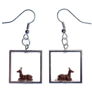 May include: Silver dangle earrings with a square frame and a small brown deer figurine inside each frame.