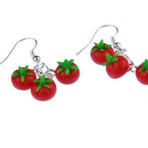 Puede incluir: Un par de pendientes de plata con tres colgantes de tomate rojo en cada pendiente. Los tomates tienen hojas verdes.