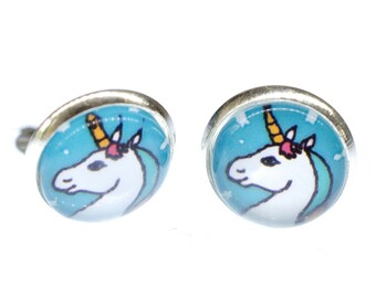 Könnte beinhalten: Ein Paar silberne Ohrstecker mit blauem Hintergrund und einem weißen Einhorn mit gelbem Horn und rosa Blumen auf dem Kopf.