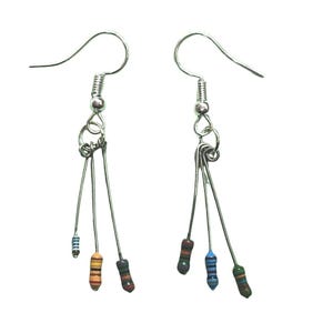 Pode incluir: Um par de brincos de prata com três resistores pendurados. Os resistores são de cor laranja, preto e azul em um brinco e azul, verde e preto no outro.