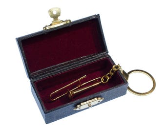 May include: A miniature gold-colored trombone keychain resting inside a small, rectangular, dark blue box with a hinged lid and a deep red velvet-lined interior. The box features a metallic latch closure and a gold-toned metal ring attachment.