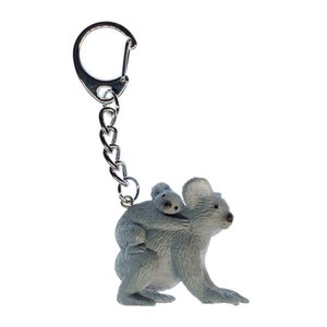 Könnte beinhalten: Ein grauer Koalabären-Schlüsselanhänger mit einem Baby-Koala auf dem Rücken. Der Schlüsselanhänger ist aus Kunststoff und hat eine silberne Metallkette.