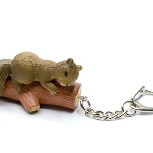 Puede incluir: Un llavero de ardilla marrón con un diseño esculpido detallado. La ardilla está posada en un tronco marrón con una cadena plateada.