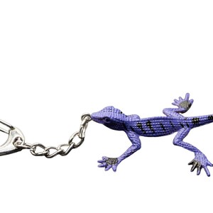 May include: A purple lizard keychain featuring a textured body with black horizontal stripes along the back and dark gray accents on the feet. The lizard is attached to a silver-toned metal split ring by a short silver-toned metal chain link.