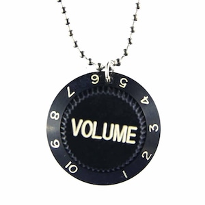 Op de afbeelding: Een zwarte metalen ketting met een ronde hanger waarop het woord "VOLUME" staat. De hanger heeft nummers van 1 tot en met 10 rond de rand.