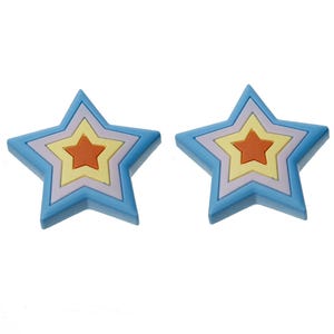 May include: Two star-shaped ornaments featuring a layered design. Each star consists of a bright blue outer layer, a light purple middle layer, a pale yellow inner layer, and a solid orange star at the very center, creating a nested appearance.
