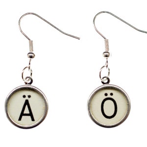 Peut inclure: Une paire de boucles d'oreilles en argent avec des touches de machine à écrire représentant les lettres "Ä" et "Ö".