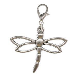 Könnte beinhalten: Silberfarbener Libellen-Anhänger mit Clipverschluss. Die Libelle hat ein detailliertes Design mit zarten Flügeln und einem langen, schlanken Körper.
