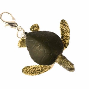Könnte beinhalten: Ein grüner und brauner Meeresschildkröten-Schlüsselanhänger mit einem silbernen Metallverschluss. Die Schildkröte ist aus Kunststoff und hat eine detaillierte Schale und Flossen.