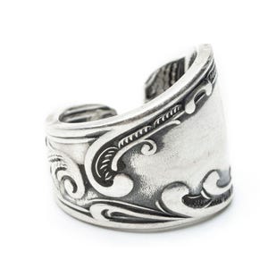 May include: A silver ring with an intricate, swirling design. The ring is open on one side and has a smooth, polished finish.