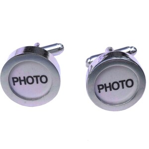 May include: A pair of silver cufflinks featuring a white circular face with the word "PHOTO" printed in black. The cufflinks have a shiny, metallic finish and a classic design, suitable for formal wear.