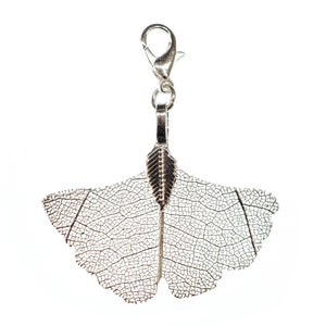 May include: Silver charm featuring a detailed ginkgo leaf design. The charm has a silver loop for attaching to a bracelet or necklace.