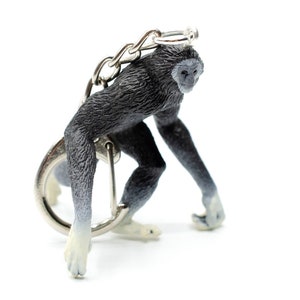Peut inclure: Un porte-clés en forme de singe noir et blanc avec une chaîne argentée. Le singe est en position accroupie, les bras tendus.