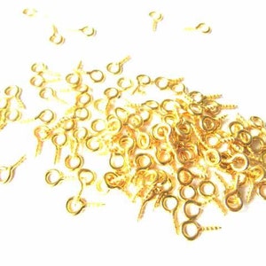 Può includere: Un grande mucchio di ganci ad occhiello dorati a vite. Gli occhielli sono piccoli e rotondi, e le viti sono corte e sottili.