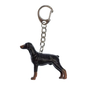 May include: Black and tan Doberman Pinscher dog keyring. The dog is standing on all four legs with its head turned to the left. The keyring is attached to a silver chain and ring.