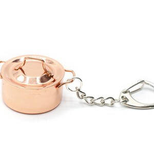 May include: A copper pot keychain with a silver chain and ring. The pot has a lid with a handle.