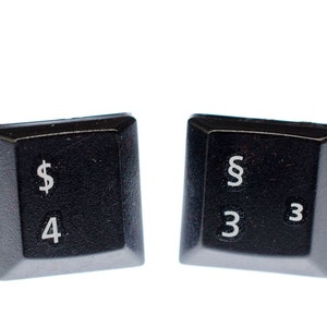 May include: Two black plastic keyboard keys with white lettering. The first key has a dollar sign and the number four. The second key has the section symbol and the number three repeated.