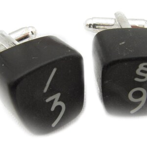 May include: A pair of black cufflinks shaped like computer keys. One cufflink has the number "3" and a slash on it. The other cufflink has the number "9" and a paragraph symbol on it.