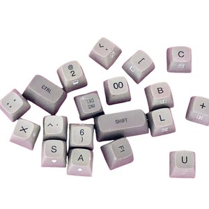 May include: A collection of gray plastic keys with various letters, numbers, and symbols printed on them. The keys are arranged in a random pattern on a white background.