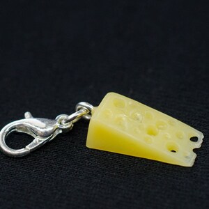 Peut inclure: Un charme en argent en forme de morceau de fromage suisse avec des trous. Le charme est attaché à un fermoir à homard en argent.