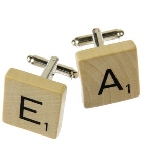 May include: A pair of wooden cufflinks shaped like Scrabble tiles. The left cufflink has the letter "E" with a score of 1. The right cufflink has the letter "A" with a score of 1.