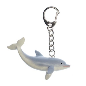 May include: A silver keychain with a gray dolphin charm. The dolphin is facing right and has a slightly open mouth. The keychain is made of metal and has a silver chain.