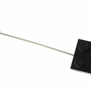 May include: A black Lego brick pin with a silver pin back. The brick has four studs.