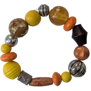 Könnte beinhalten: Ein farbenfrohes Perlenarmband mit einer Mischung aus Holz-, Glas- und Metallperlen. Das Armband hat gelbe, orange, braune und silberne Perlen.