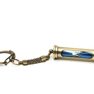 May include: A gold-toned hourglass keychain with a blue and white hourglass inside. The keychain has a metal chain and a ring.