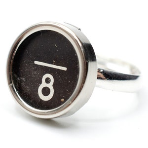 Puede incluir: Un anillo de plata con una tecla de máquina de escribir negra con el número 8.