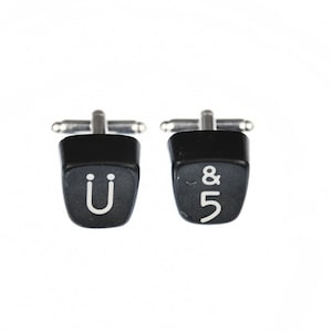 May include: A pair of black cufflinks shaped like typewriter keys. The left cufflink has the letter "U" on it, and the right cufflink has the ampersand symbol and the number "5" on it.