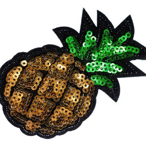 Può includere: Un toppa di ananas con paillettes dorate e verdi. L'ananas è fatto di paillettes dorate e le foglie sono fatte di paillettes verdi.