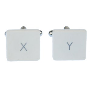 May include: A pair of white cufflinks with silver accents. The cufflinks are shaped like computer keys, with the letters "X" and "Y" printed on them.