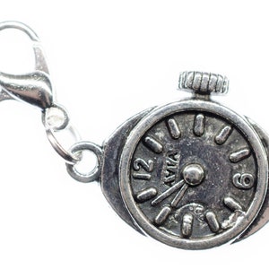 May include: A silver-toned charm in the shape of a vintage watch. The watch face displays the time with the numbers 12 and 9 visible. The charm includes a clasp for easy attachment. The word "AVIA" is printed on the watch face.