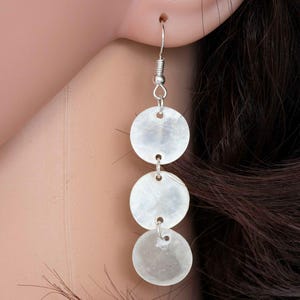 May include: White shell earrings with three round discs hanging from a silver hook.