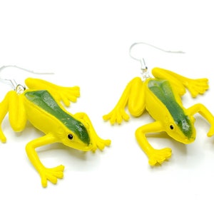 Könnte beinhalten: Ein Paar gelbe Frosch-Ohrringe mit grünen Akzenten. Die Frösche hängen an silbernen Haken.