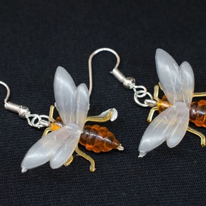 May include: A pair of silver bee earrings with translucent white wings and amber-colored bodies.