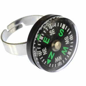 May include: A black compass ring with a green needle and white markings for the cardinal directions. The ring is made of silver metal.