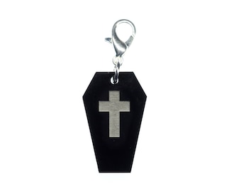 May include: Black coffin-shaped keychain with a silver cross on the front. The keychain has a silver clip.