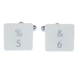 May include: A pair of white ceramic cufflinks with silver accents. The left cufflink has a percentage symbol and the number 5. The right cufflink has an ampersand symbol and the number 6.