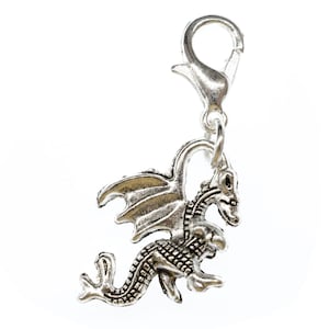 May include: Silver charm featuring a detailed dragon with wings and a textured body. The charm has a lobster clasp for attaching to a bracelet or necklace.